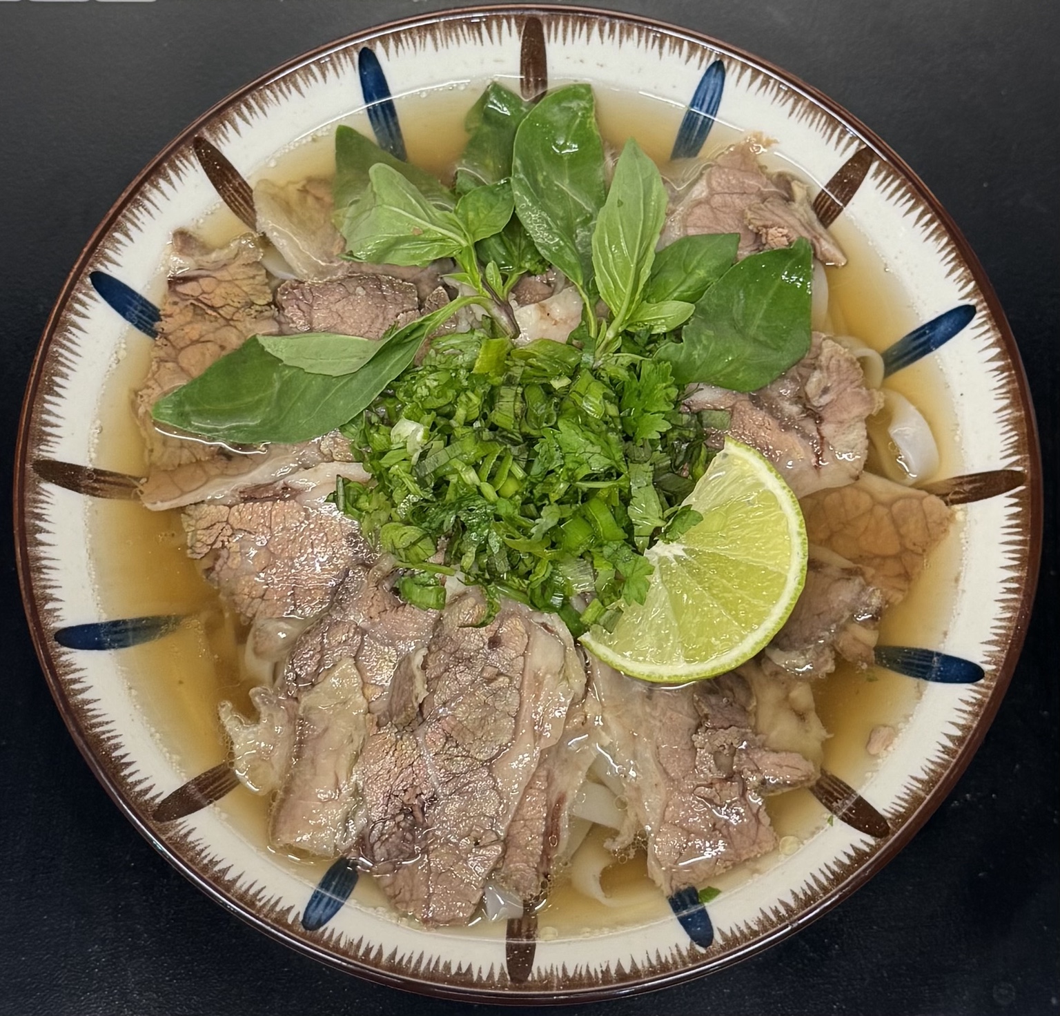 A bowl of Vietnamese beef pho with fresh herbs and lime